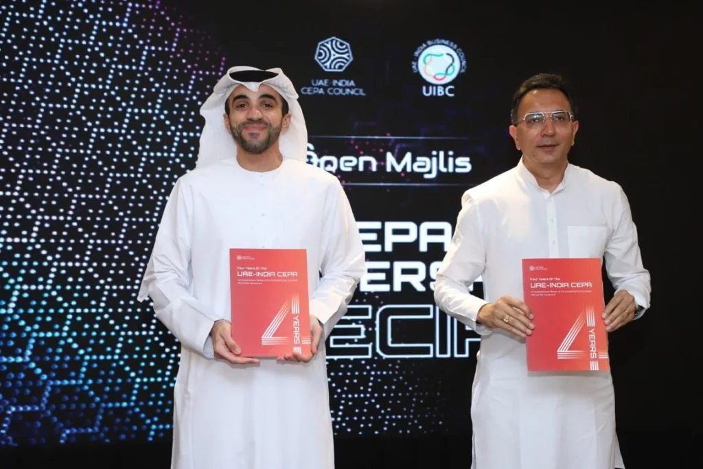 Two people on stage holding up copies of a red publication, in front of the LED loop with the Council and UIBC marks above them.
